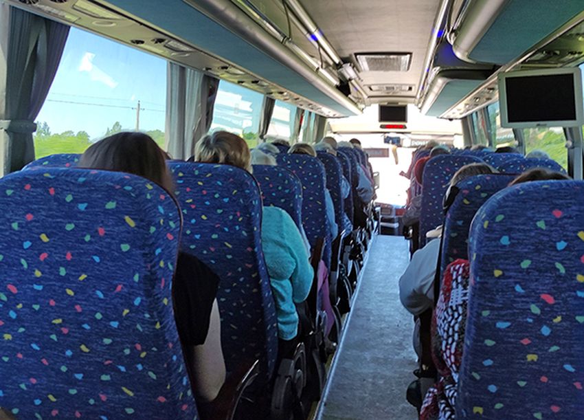 внутри автобуса. вид с задней площадки автобуса. на пассажирских креслах синего цвета сидят участники экскурсии.