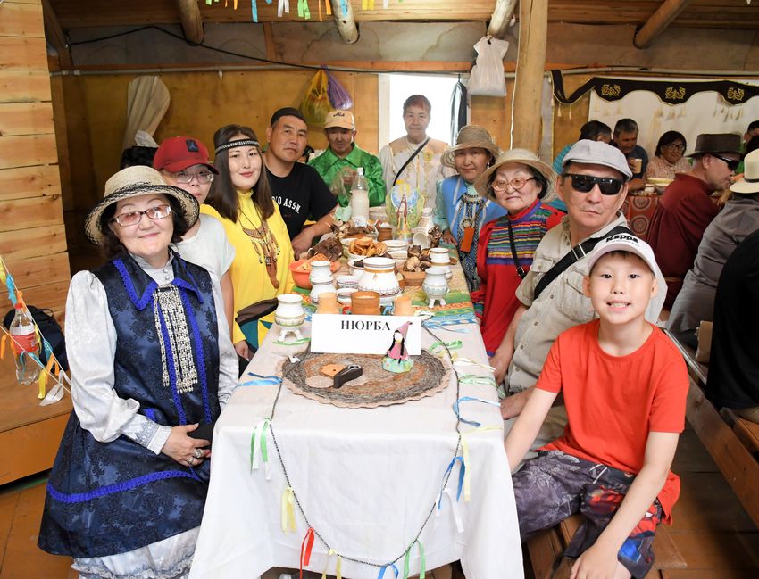 за столом с белой скатертью сидят члены якутской ро вос и гости, некоторый в национальных костюмах, на столе сладости и сосуды на трех ножках (чороны). справа видно, что рядом люди сидят еще за двумя столами