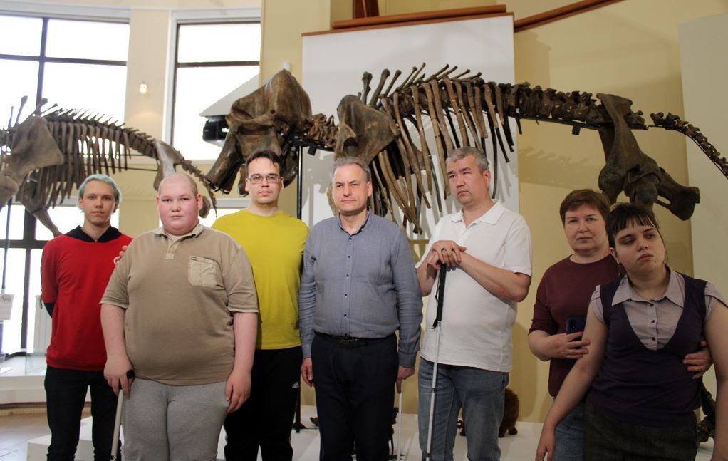 Участники занятий на экскурсии в музее. За ними большие скелеты динозавров.