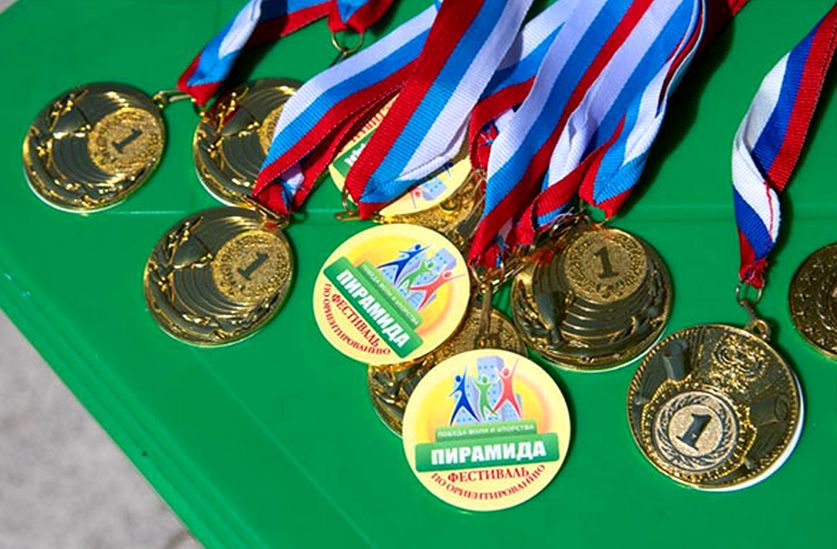 на зеленом сукне лежат медали за первые места в разных дистанциях. медали на шнурке расцветкой триколор 