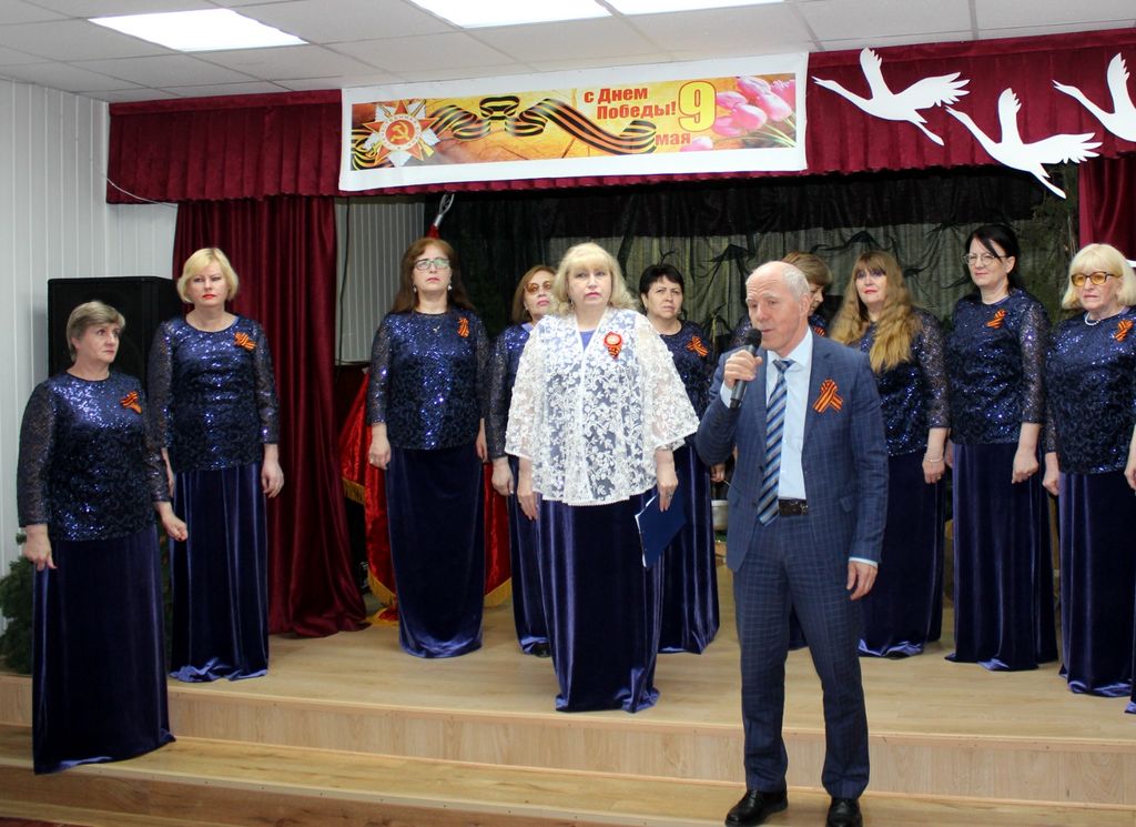 На сцене участники хорового коллектива "Гармония" - женщины в платьях тёмно-фиолетового цвета. На сцене также председатель Карачаево-Черкесской РО С. М. Дубовик с микрофоном в руке.