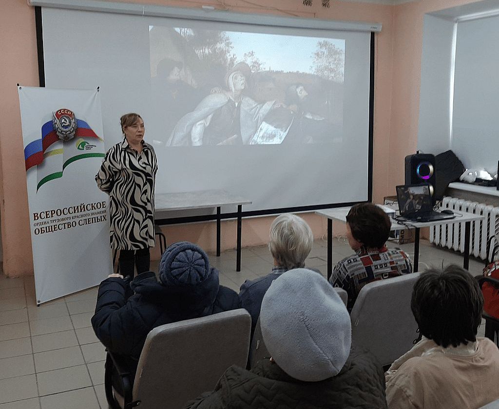 На экране - кадры из фильма, рядом стоит женщина. Зрители в зале