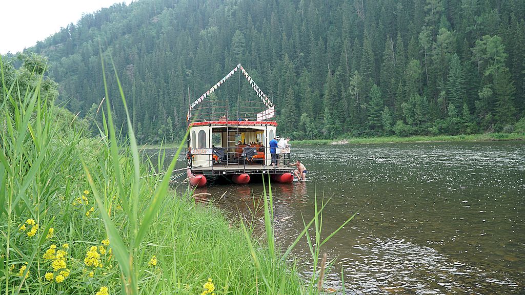 Фотография с берега. По реке плывёт паром с участниками сплава.