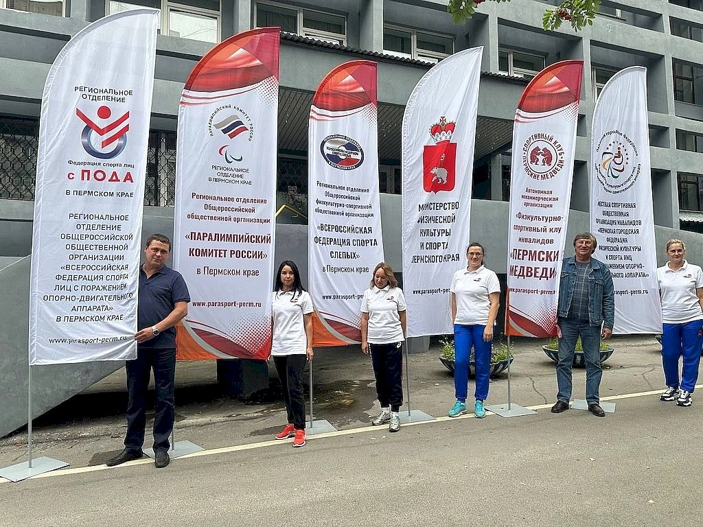 На фотографии спортсмены стоят около флагов Федерации спорта слепых