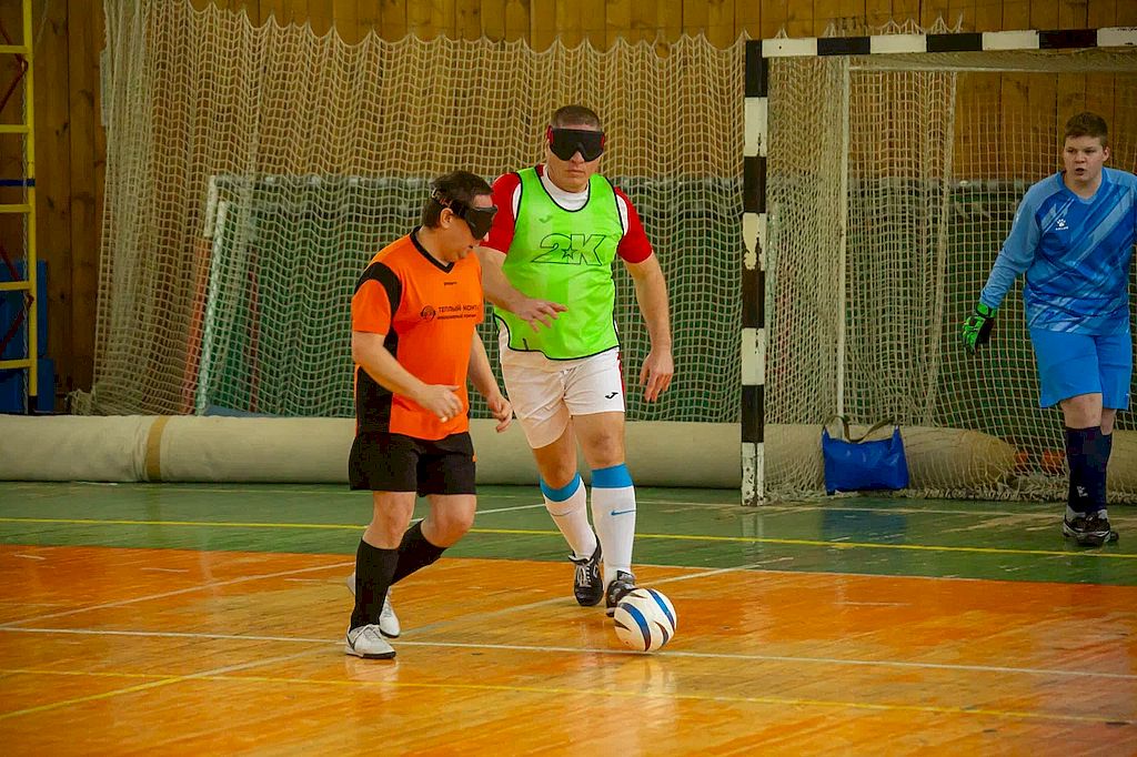 момент игры.. На поле два игрока в повязках на глазах. Перед одним из них мяч