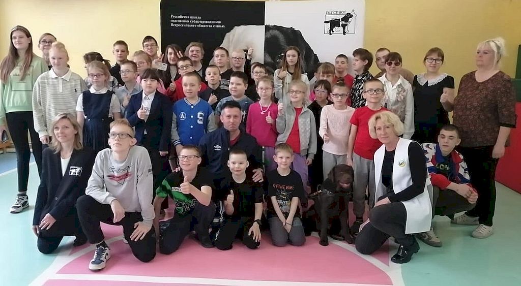 Участники и организаторы мероприятия на фоне баннера Российской школы подготовки собак-проводников ВОС.