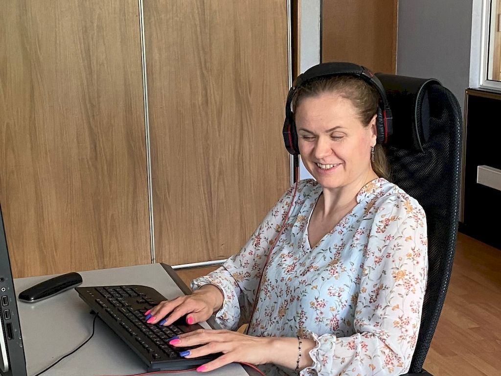 Юлия Емельянова за рабочим местом. Она положила руки на клавиатуру и улыбается