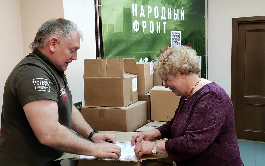 В. И. Прудкова с мужчиной в футболке и жилетке с надписью: "Народный фронт" упаковывают посылки для бойцов СВО.