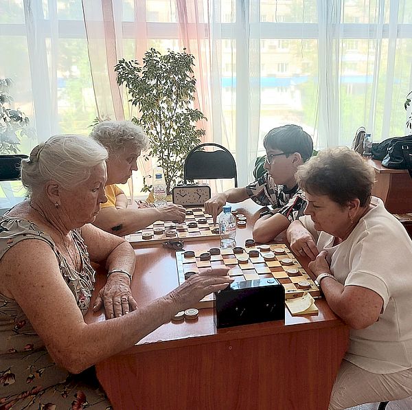 Игровой момент. Четыре женщины сидят друг напротив друга. Между ними доски с шашками.