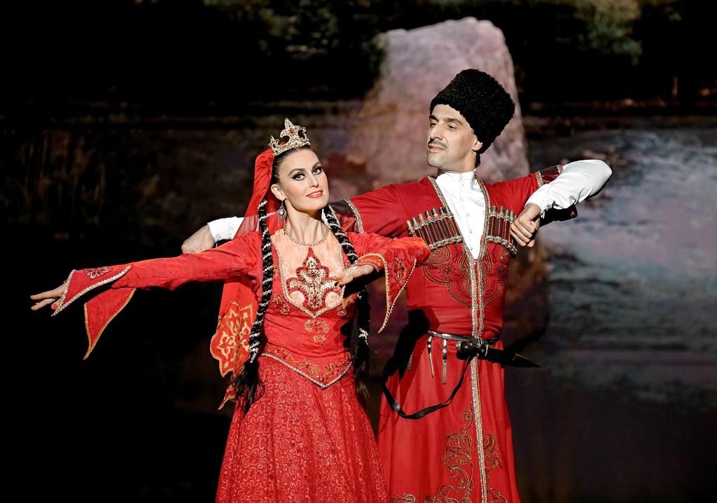 На сцене танцующая пара мужчина и женщина в красных национальных костюмах.