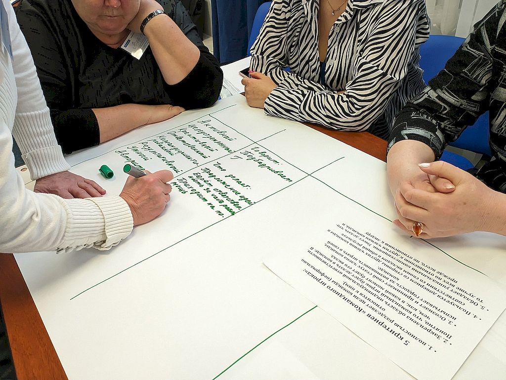 на фотографии участники семинара делают записи на большом листе зелёным маркером