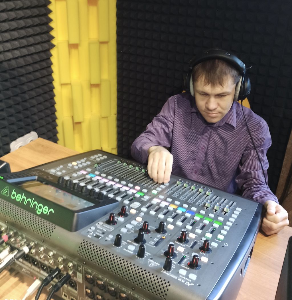 Член Тюменской РО ВОС в должности звукорежиссёра: незрячий молодой человек в студии звукозаписи сидит за микшерным пультом. Он в наушниках, правой рукой регулирует настройки на пульте.