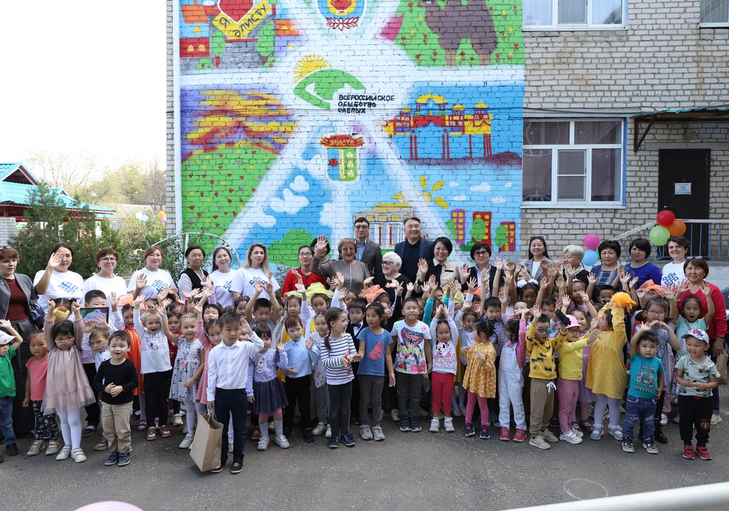 Представители Калмыцкой РО ВОС и воспитанники детского сада на фоне граффити из их рисунков на стене здания